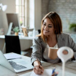 Happy businesswoman writing notes while working on laptop in the